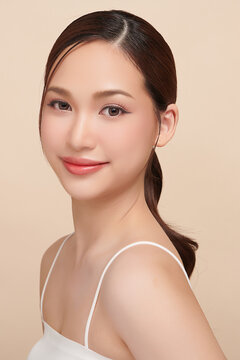 A beautiful young Asian woman with clean, fresh skin against a beige background. Skincare, facial treatment, cosmetology, beauty, and spa. An elegant portrait of an Asian woman.