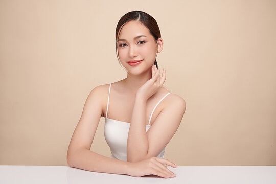 A beautiful young Asian woman with clean, fresh skin against a beige background. Skincare, facial treatment, cosmetology, beauty, and spa. An elegant portrait of an Asian woman.