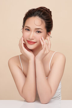 A beautiful young Asian woman with clean, fresh skin against a beige background. Skincare, facial treatment, cosmetology, beauty, and spa. An elegant portrait of an Asian woman.