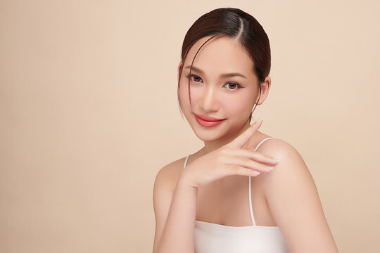 A beautiful young Asian woman with clean, fresh skin against a beige background. Skincare, facial treatment, cosmetology, beauty, and spa. An elegant portrait of an Asian woman.