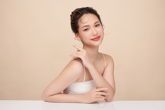 A beautiful young Asian woman with clean, fresh skin against a beige background. Skincare, facial treatment, cosmetology, beauty, and spa. An elegant portrait of an Asian woman.