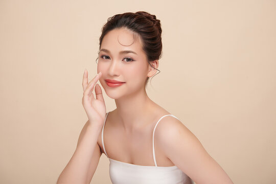 A beautiful young Asian woman with clean, fresh skin against a beige background. Skincare, facial treatment, cosmetology, beauty, and spa. An elegant portrait of an Asian woman.