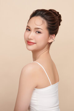 A beautiful young Asian woman with clean, fresh skin against a beige background. Skincare, facial treatment, cosmetology, beauty, and spa. An elegant portrait of an Asian woman.