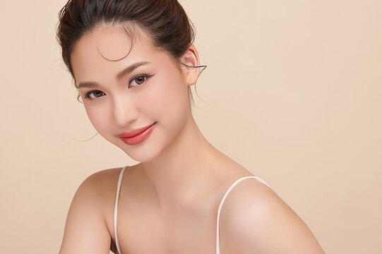A beautiful young Asian woman with clean, fresh skin against a beige background. Skincare, facial treatment, cosmetology, beauty, and spa. An elegant portrait of an Asian woman.