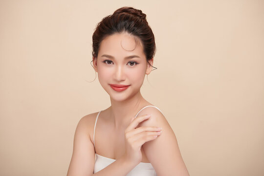 A beautiful young Asian woman with clean, fresh skin against a beige background. Skincare, facial treatment, cosmetology, beauty, and spa. An elegant portrait of an Asian woman.