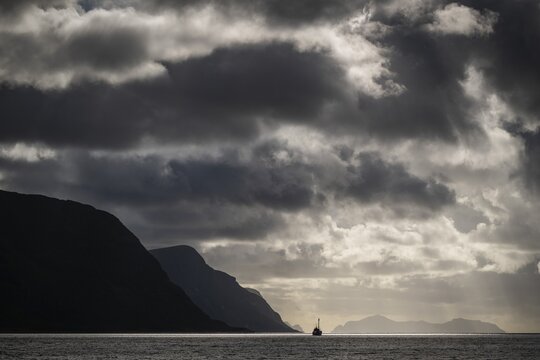 Dramatic lighting and dark clouds over the sea, island, ship, near &Aring;lesund or Alesund, M&oslash;re og Romsdal Fylke, Norway