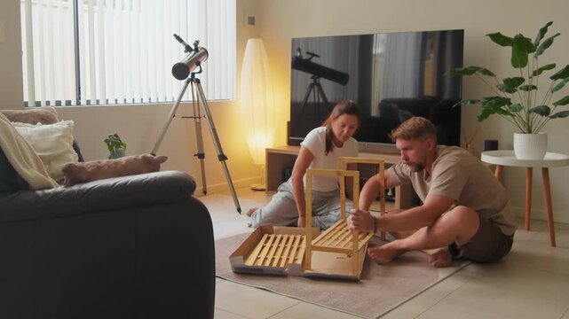 Young man and woman working together to assemble a wooden shelf unit in their bright living room during the afternoon at home