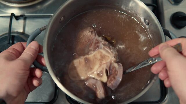 Person stirring beef shank in a pot of boiling broth