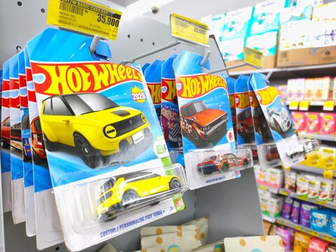 Malang, Indonesia - July 18, 2026: Multiple packaged Hot Wheels die-cast cars hanging on display hooks at a store shelf, featuring yellow, orange, and white models.