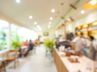 Fotobehang Horeca Blurred cafe interior with coffee bar counter, warm lighting, and customers in soft focus, creating a cozy background for hospitality, restaurant, coffee shop, lifestyle, and copy space.  © tete_escape