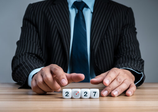 Business executive arranges white 2027 blocks with a bullseye replacing zero on desk, representing corporate goal setting, strategic focus, annual planning, leadership and measurable success concept.