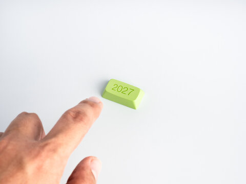 Finger approaches a green 2027 key on a clean white background with copy space. Future planning, strategic decisions, business activation, annual transition and the start of new goals concept.