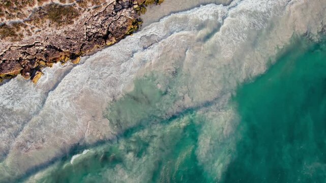 Aerial view of white waves crash against the rocky shoreline of the Indian ocean creating foam in the shallow waters of the coast of Australia