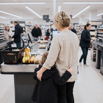 Mother hugs child at supermarket checkout with groceries in baskets