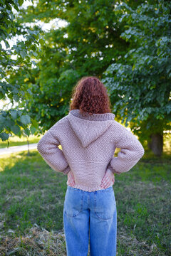 Redhead teenage girl in chunky knit sweater with hood back view, outdoors. Bulky knitwear, clothing and style concept