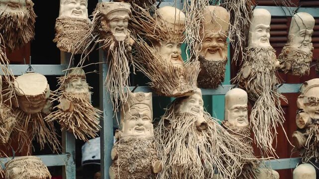 Traditional wooden busts with painted faces and fibrous hair displayed on blue crates at an outdoor market in Hoi An, Vietnam during daytime.
