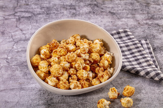 Caramel popcorn in white bowl with checkered napkin on stone table