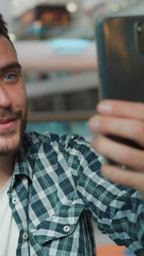 Happy smiling Caucasian man influencer talking video call with mobile phone in shopping mall cheerful male blogger talk chatting online conference with smartphone recording blog social media stream