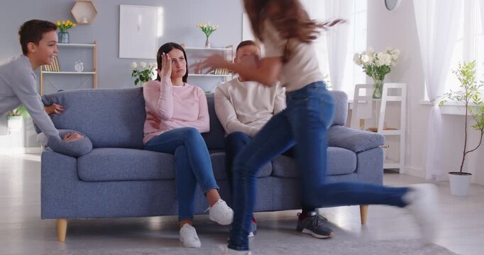Parents feeling tired and unhappy as kids playing loudly, misbehave, and create chaos at home. The stressful atmosphere highlights noise, parenting challenges, and daily family struggles.