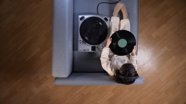 Person wearing headphones and lying on a couch, holding a vinyl record while a turntable is next to them, enjoying music and a relaxed atmosphere