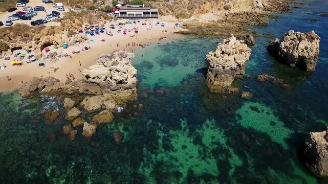 Beautiful aerial view flying away from the stunning praia dos arrifes, a golden sand beach nestled among ochre colored cliffs with crystal clear turquoise water in albufeira, algarve, portugal
