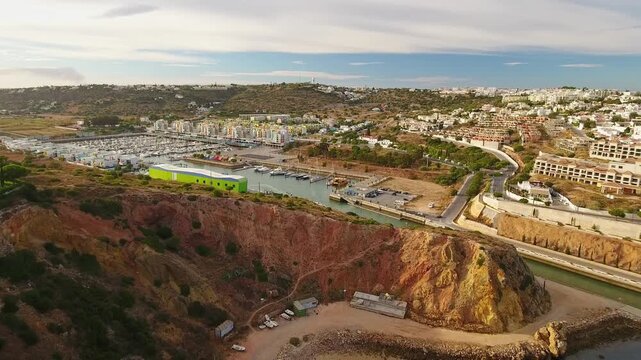Aerial view flying over the scenic albufeira marina, showcasing the beautiful red cliffs, the narrow entrance channel, and the picturesque coastal town in the sunny algarve region of portugal