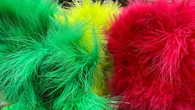 A vibrant close-up macro shot featuring fluffy, brightly dyed green, yellow, and red feathers or long-pile faux fur creating a soft, colorful, and playful abstract texture.