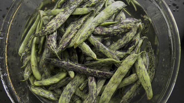 Removing black sieve to reveal green bean pods in water glass bowl, 4K