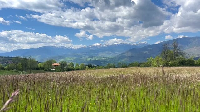 Scenic view of rolling hills, mountains, and a cloudy sky under sunlight. Mountain range with wildflowers. Landscape with Rolling Hills and Cloudy 