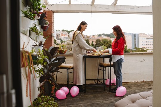 Two female friends setting table at a birthday party on an apartment b