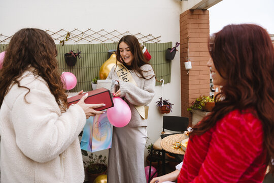 Two female friends opening gift at a birthday party on an apartment ba