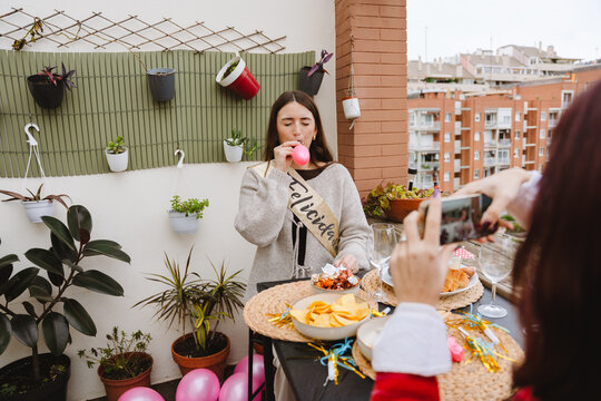 Two female friends blowing balloon at a birthday party on an apartment