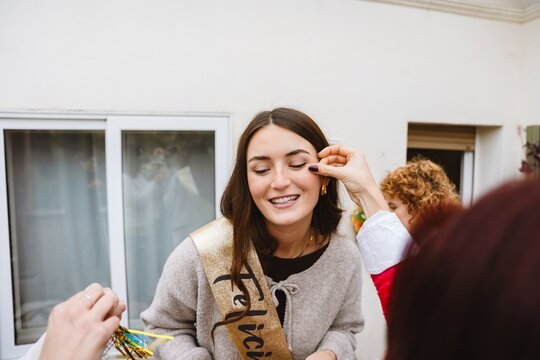 Two female friends placing a face decoration on a friend at a birthday