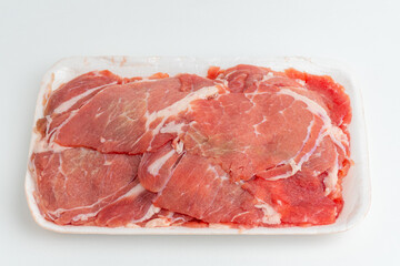 Fototapeta premium Fresh thinly sliced raw red meat in white plastic packaging tray isolated on white background