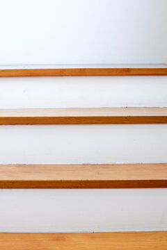 Vertical shot of wooden stairs with clean white risers. A minimalist interior design featuring strong horizontal lines, authentic natural wood texture, and soft natural light for background.