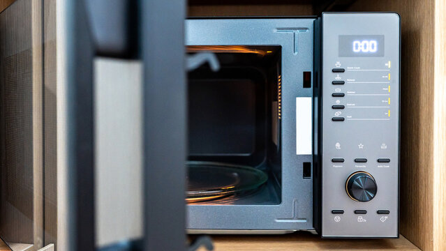 Empty microwave oven with open door. Digital timer display, mode buttons and knob on control panel. Home appliance in the kitchen