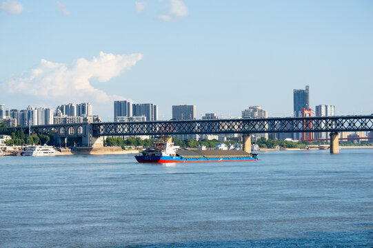 A large cargo ship sails on the Yangtze River under the main bridge in the city of Wuhan China with a modern urban skyline in the background