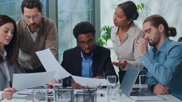 African American businessman leader with multiracial business team talking conversation analyze papers documents diversity five agents entrepreneurs brainstorming working at company office meeting