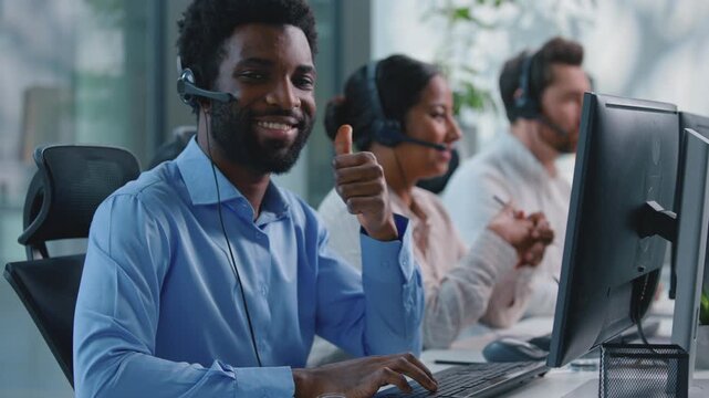 Happy African American business man operator showing thumb up talking with client call center computer chat smile businessman looking at camera with like in callcenter near multiethnic business team