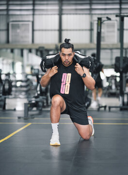 Man doing lunges with weighted bag in gym