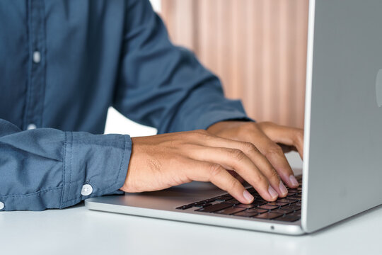 Close-up of a businessman typing on laptop computer keyboard at white desk, representing digital business strategy, software development, data entry, email communication, and office work