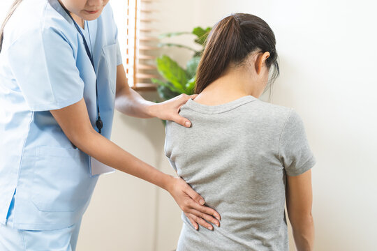 Asian young woman physical therapist examining and massaging a patient lower back for spine rehabilitation, back pain relief and office syndrome occupational therapy concept.