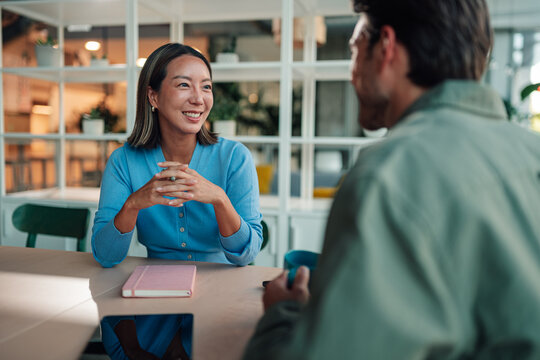 Asian businesswoman smiling during a business meeting, collaborating with a colleague in a modern office environment