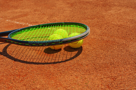 A yellow tennis ball and tennis racket lies on the clay court.