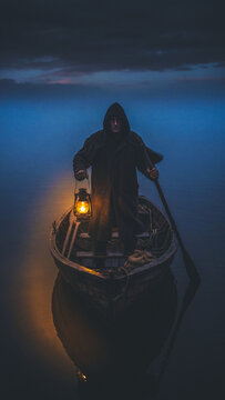 Halloween figure in boat holding lantern on misty water