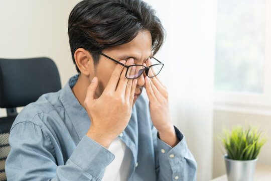 Eye problem concept, fatigue asian young man tired eyes, irritated rubbing eye dry relief vision pain after work on laptop computer, eye strain, while wearing glasses, suffer migraine, bad blurry.
