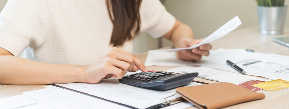 Stressed asian young business woman, employee using calculator to calculate expenses of monthly, hand holding bills and receipt for to payment on table at home. Financial, finance of banking concept.