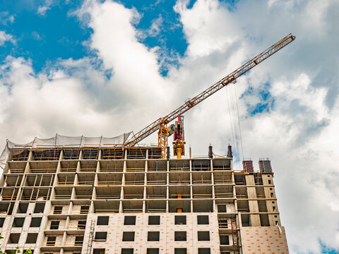 Modern residential building under construction with industrial tower crane against blue sky. Construction site and real estate development concept.