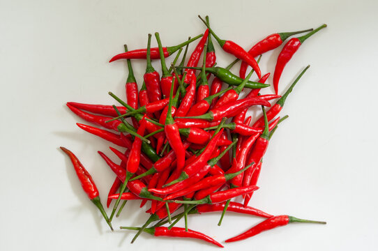 Fresh red chili peppers piled on a white background with two green peppers creating natural contrast. Minimal food flat lay with vibrant color, copy space and culinary appeal for commercial design.