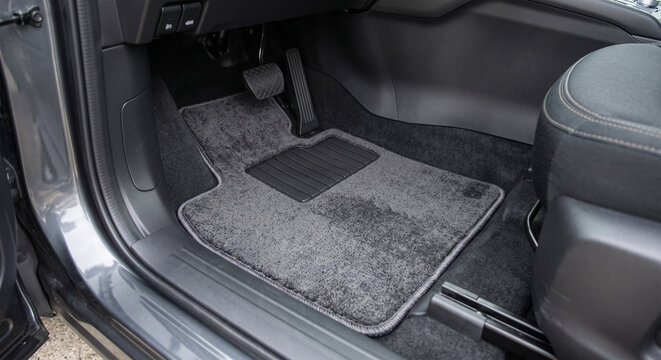 Car interior featuring a gray carpet floor mat with a textured surface and a rubber heel pad, positioned in the driver's side footwell of a modern vehicle